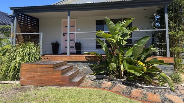 Une maison moderne dotée d’un porche abrité, d’un escalier menant à l’entrée et d’un jardin bien entretenu où poussent différentes espèces de plantes.