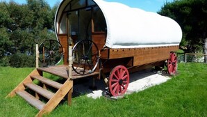A covered wagon with a wooden ramp and red wheels, parked on a grassy field.