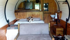 A cozy tented room with a bed, a wooden bench, a small table, and a hanging light fixture.