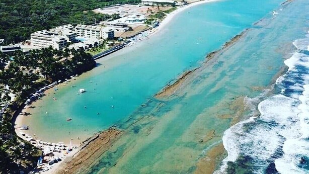 Vue aérienne d’une station balnéaire dotée d’une longue plage, d’un port de plaisance et d’une végétation luxuriante.