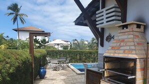 Un jardin avec un four en briques, une piscine et un espace patio aménagé avec des chaises et une table.