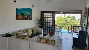 Un salon avec un canapé, un tableau et une vue sur une piscine et un jardin.