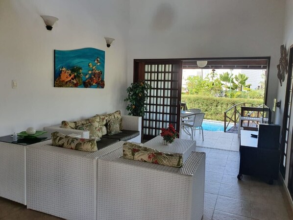 A living room with a sofa, a painting, and a view of a pool and garden.