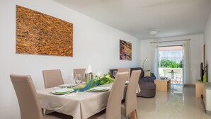 Zona pranzo con tavolo imbandito per quattro persone, sedie e un divano sullo sfondo.