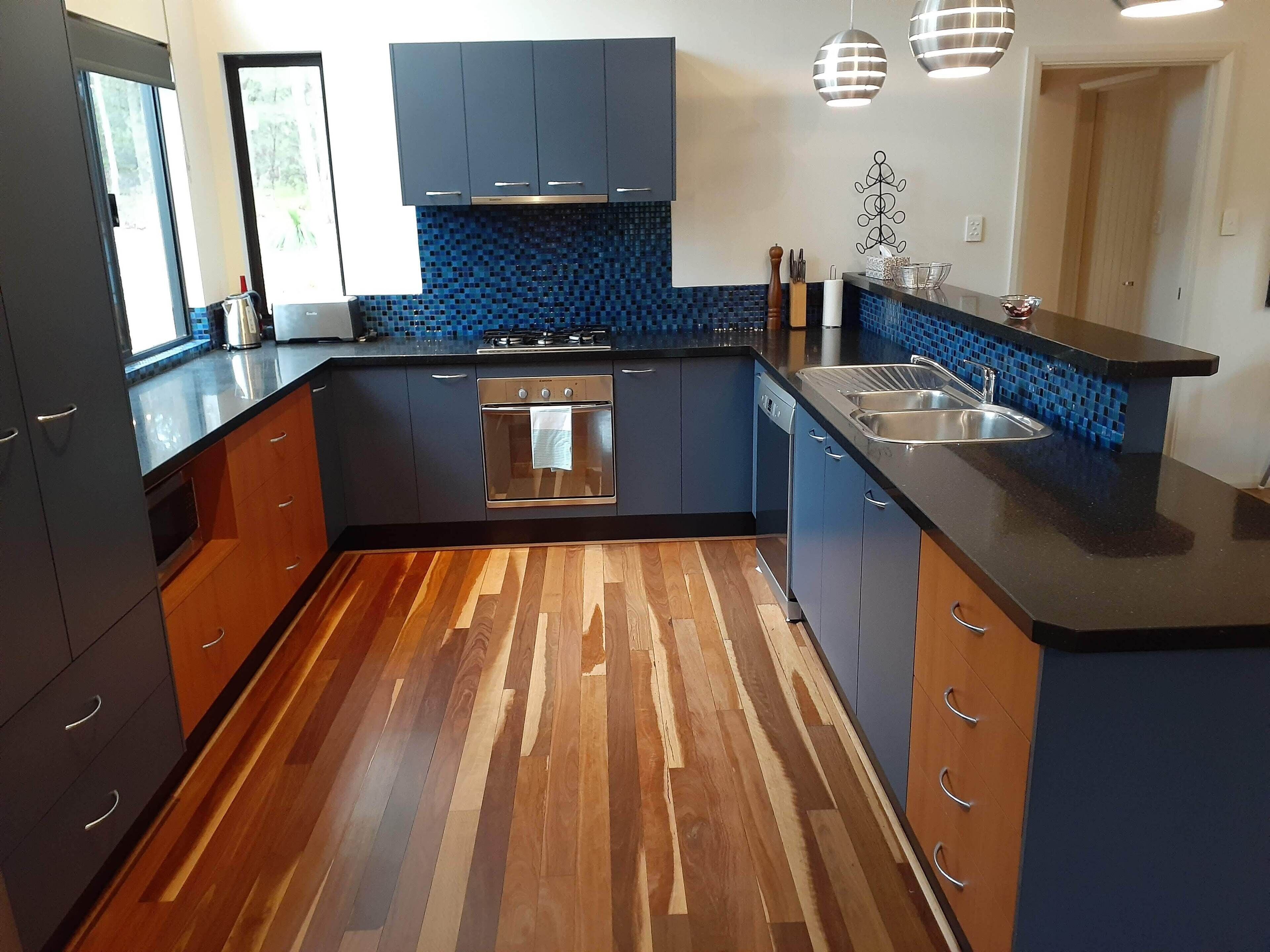 A modern kitchen with dark cabinets, a wooden floor, a stove, and a sink.