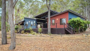 Une cabane à deux étages, à l’extérieur rouge et bleu, entourée d’arbres et dont le sol est recouvert de feuilles mortes.
