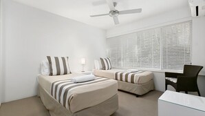A hotel room with two beds, a ceiling fan, a window with blinds, a desk, and a chair.