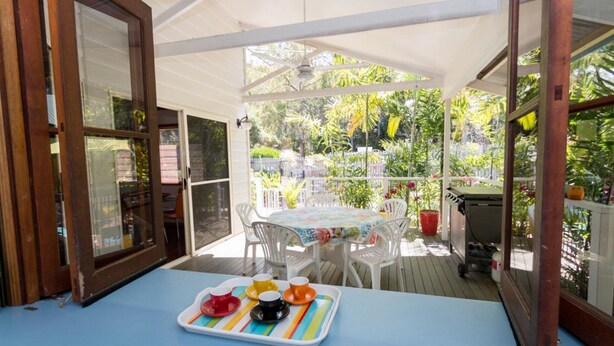 A covered patio with a table set for four, surrounded by white chairs, and a grill in the background. - Magnetic Dreams Unit 1 (ARCADIA)