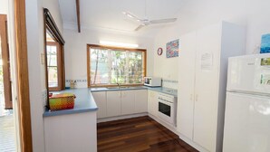 A compact kitchen with white cabinets, a microwave, a refrigerator, and a window providing natural light. - Magnetic Dreams Unit 1 (ARCADIA)