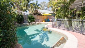 A swimming pool with a stone border, surrounded by a fence and lush greenery. - Magnetic Dreams Unit 1 (ARCADIA)
