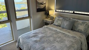 Une chambre à coucher comprenant un lit, une table de chevet, une lampe, un tableau et une fenêtre donnant sur l’extérieur.