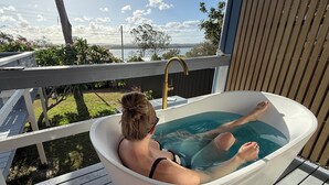 Une personne se détend dans un bain à remous sur une terrasse, avec vue sur l’eau et les montagnes.