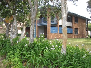 A two-story building with a balcony, surrounded by trees and flowering plants. - Aluna Holidays @ Boomerang - walk across the road to Boomerang Beach (north end) (Boomerang Beach)