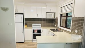 Een moderne keuken met witte kastjes, een magnetron, een fornuis en een spoelbak. Er staan twee barkrukken bij het eiland.
