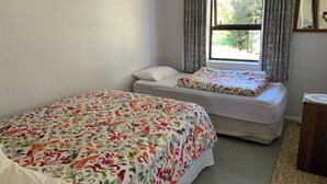 Ein Schlafzimmer mit zwei Betten, einem Fenster mit Vorhängen, einem Nachttisch und einem Spiegel.