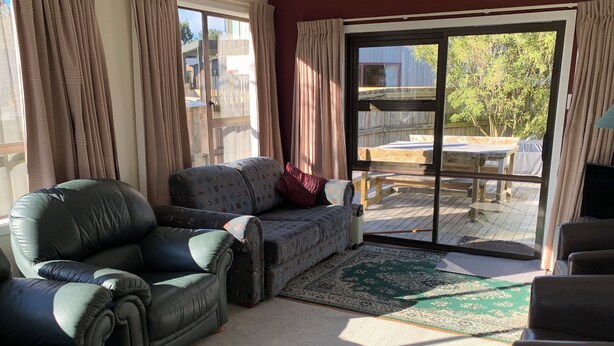 Ein Wohnzimmer mit einer Couch, einem Sessel, einem Teppich und einer Schiebetür zu einer Terrasse.