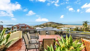 A terrace with a table and chairs, overlooking a coastal landscape with houses and a beach.