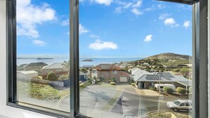 A residential area with houses, a road, and a view of the sea and hills.
