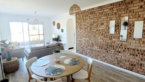 A dining area with a brick wall, round wooden table, and white chairs. - Reef Resort Apartments (Mona Vale)