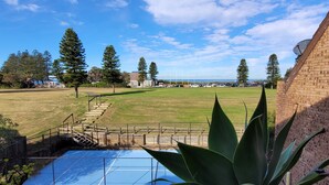 A tennis court with a blue surface, surrounded by a grassy area and trees. - Reef Resort Apartments (Mona Vale)