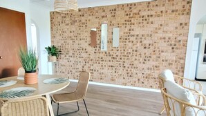 A modern dining area with a brick wall, wicker furniture, and a hanging light fixture. - Reef Resort Apartments (Mona Vale)