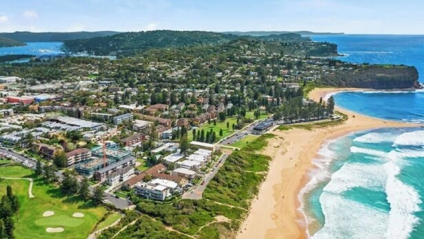 An aerial view of a coastal town with a beachfront, residential buildings, and a golf course. - Reef Resort Apartments (Mona Vale)