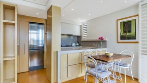Une cuisine moderne dotée d’un réfrigérateur encastré, de meubles blancs et d’un coin repas avec une table en bois et des chaises blanches.