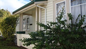 A house with a porch, a window with a curtain, and a green bush in front.