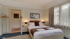 A bedroom with a bed, bedside tables, a hanging light, a picture on the wall, and a window with curtains.