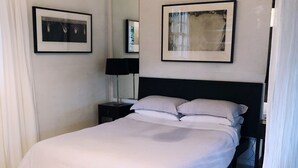 Un lit bien fait, recouvert d’une couvre-lit à rayures, une table de chevet avec une lampe et des œuvres d’art encadrées accrochées aux murs.
