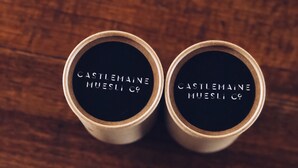 Deux récipients cylindriques portant l’inscription « CASTLEMAINE MUESLI CO », placés sur une surface en bois.