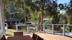 A wooden deck with a table and chairs, surrounded by a railing, overlooking a residential area with houses and trees.