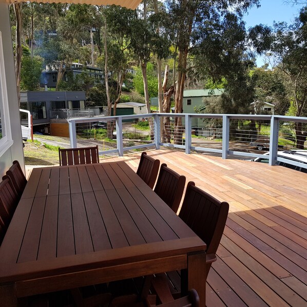 A wooden deck with a table and chairs, surrounded by a railing, overlooking a residential area with houses and trees.