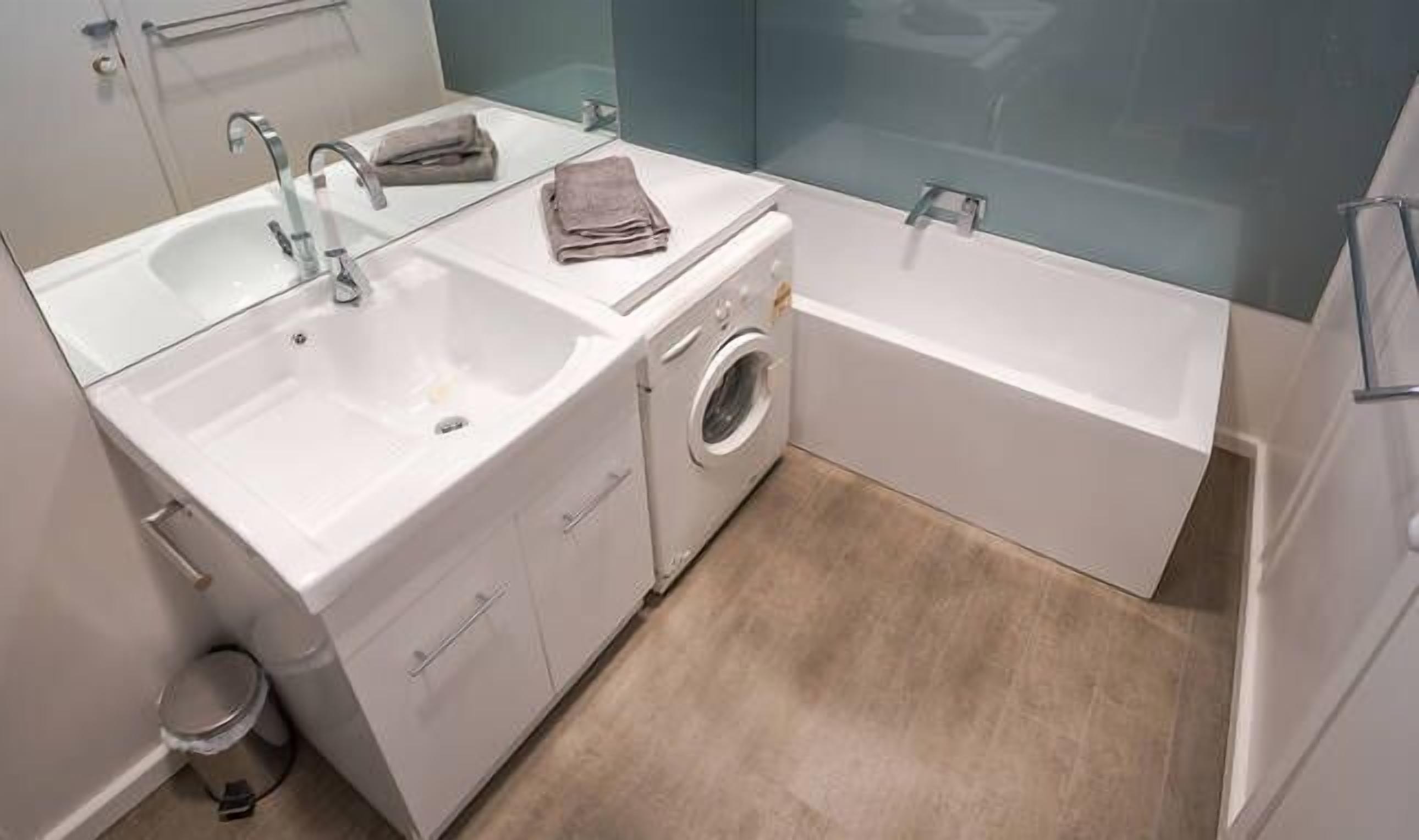 Une petite salle de bain comprenant un lavabo, un lave-linge et une baignoire.