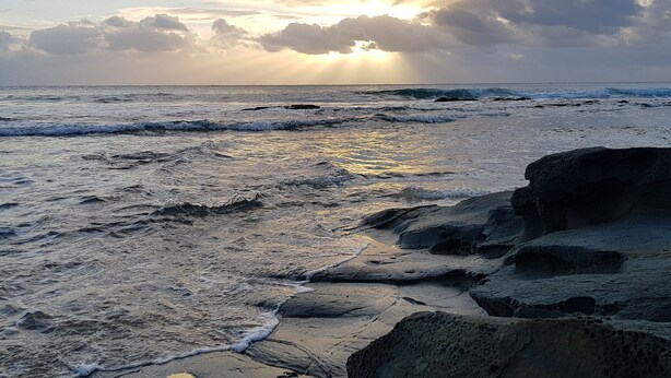 A rocky shoreline with waves and a sunset in the background.