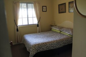 Une chambre à coucher avec un lit, une fenêtre avec des rideaux et une table de chevet avec une lampe.