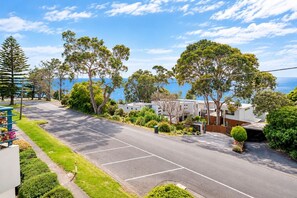 A residential street with a clear view of the sea, surrounded by trees and a parking area.