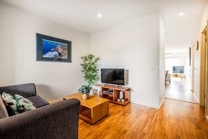 A modern living room with a sofa, coffee table, TV stand, and a large plant.