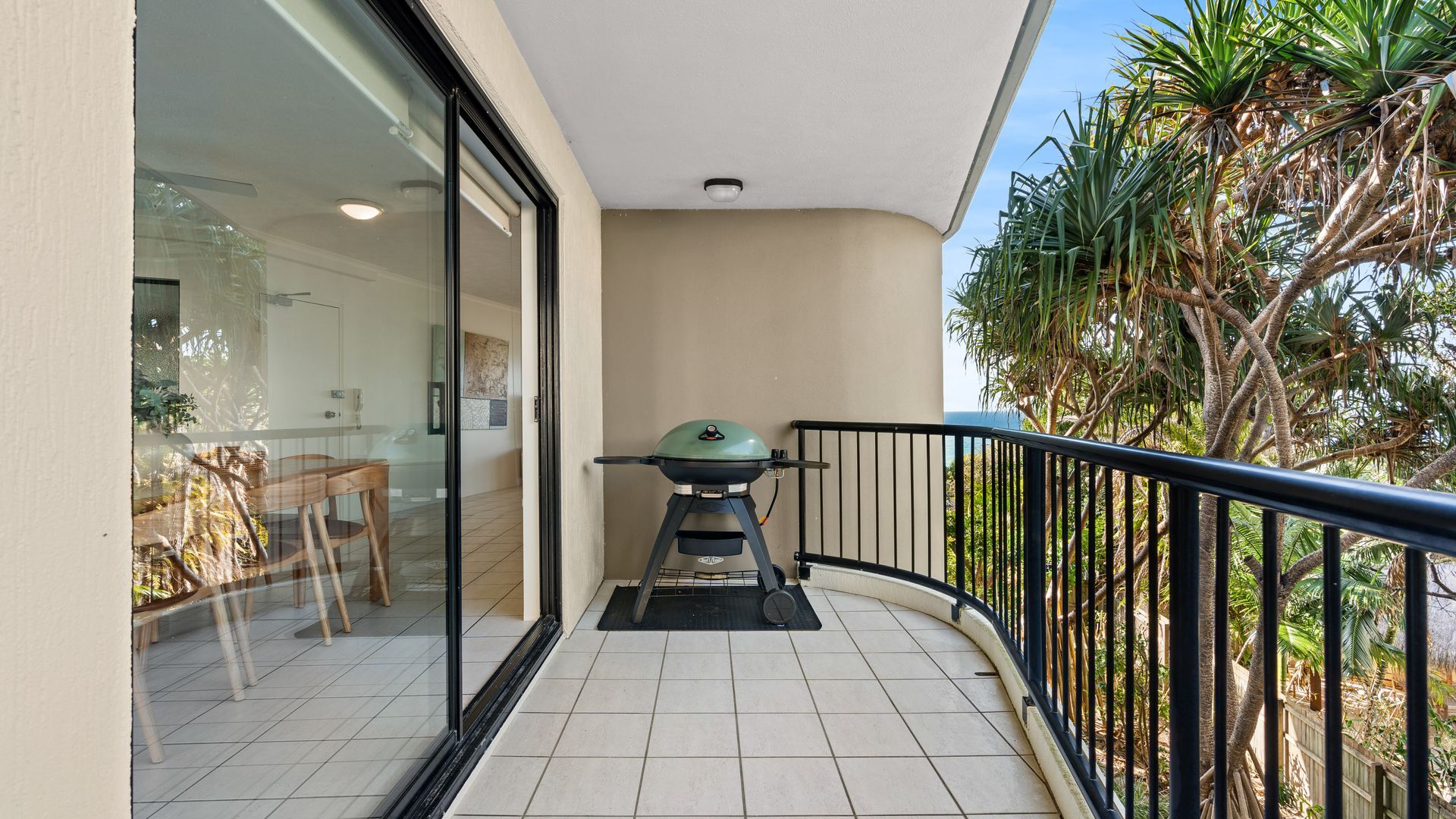 A balcony with a grill, a dining table, and chairs, overlooking a tropical garden.