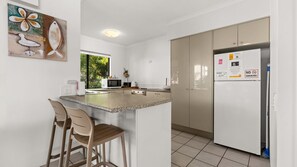 A modern kitchen with a central island, two bar stools, a microwave, and a refrigerator with a notice. - Domani - Large Townhouse with Ocean Views (Sunshine Beach)