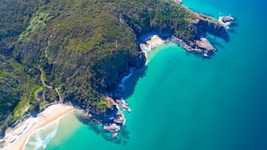 An aerial view of a coastal area with dense forest, clear turquoise waters, and a sandy beach. - Domani - Large Townhouse with Ocean Views (Sunshine Beach)