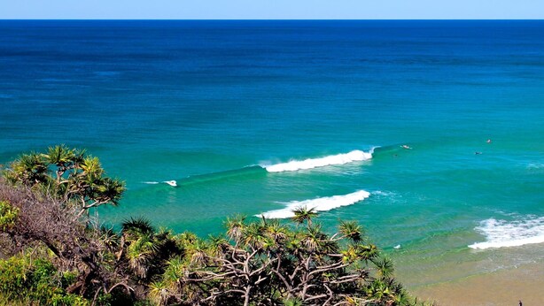 Paisaje costero con aguas azul turquesa, olas y vegetación tropical.