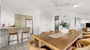 A modern dining area with a wooden table, four chairs, a vase with flowers, and a ceiling fan. - Domani - Large Townhouse with Ocean Views (Sunshine Beach)