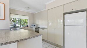 A modern kitchen with a granite countertop, stainless steel appliances, and a view of greenery outside.