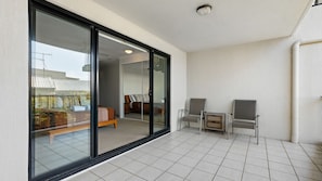 A modern room with a large sliding glass door leading to a balcony, a bed, two chairs, and a small table. - Domani - Large Townhouse with Ocean Views (Sunshine Beach)