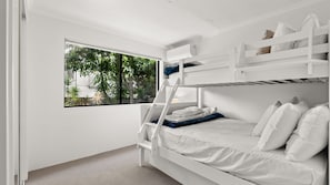 A bunk bed room with a window, white walls, and a view of greenery outside. - Domani - Large Townhouse with Ocean Views (Sunshine Beach)