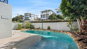 A swimming pool with a clear blue water, surrounded by a white wall and a rock border. - Domani - Large Townhouse with Ocean Views (Sunshine Beach)