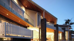 Une maison moderne à deux étages, dotée d’une façade en bois, de piliers en pierre et d’un balcon en verre.