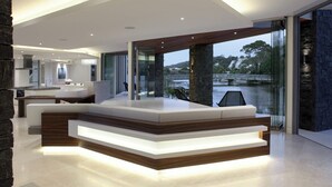 Une cuisine moderne dotée d’un îlot central, d’un coin repas avec une longue table et d’une vue sur une étendue d’eau grâce à de grandes fenêtres.