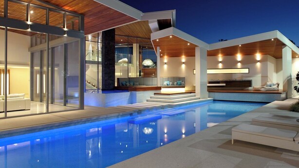 Une maison moderne dotée d’une piscine, d’un espace salon extérieur et d’un escalier menant à un étage supérieur.